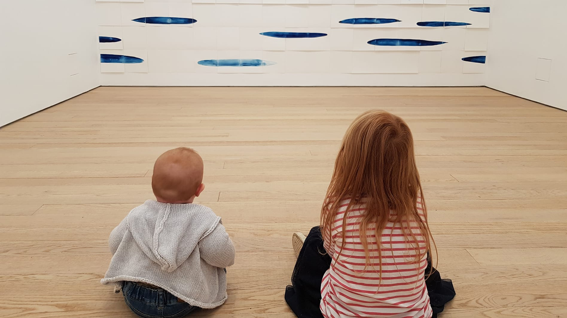 photo of two young girls sat on the floor of the gallery looking at artwork on the wall